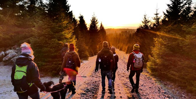 Dem Sonnenuntergang entgegen geht eine Gruppe Menschen mit Hund