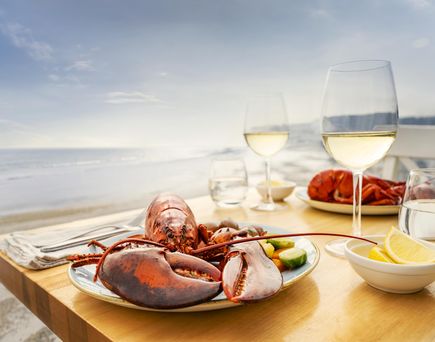 Gedeckter Tisch mit Weingläsern und Lobster am Strand mit Blick aufs Meer