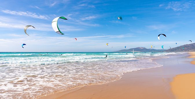 Ein Sandstrand mit türkisfarbenem Wasser und einem Kite-Surfer.