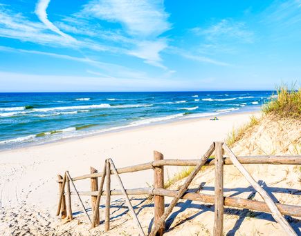 Ein Sandstrand mit blauem Meer und einem hölzernen Pier.
