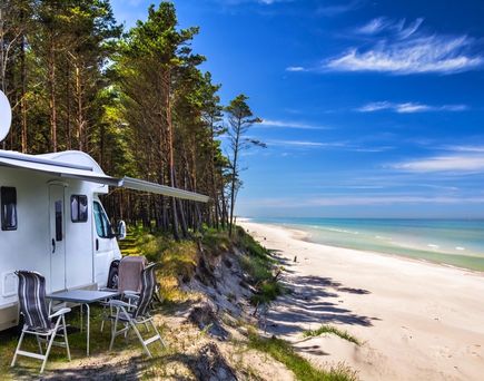 Ein Campervan parkt direkt am Sandstrand des Baltischen Meeres, umgeben von Dünen und einem kleinen Gebäude.