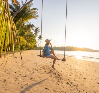 Frau sitzt auf Schaukel an einem Strand mit Meer im Hintergrund
