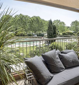 Überdachte Terrasse mit Sofa und Blick auf einen grünen Garten mit Poolanlage und gepflegter Parklandschaft.