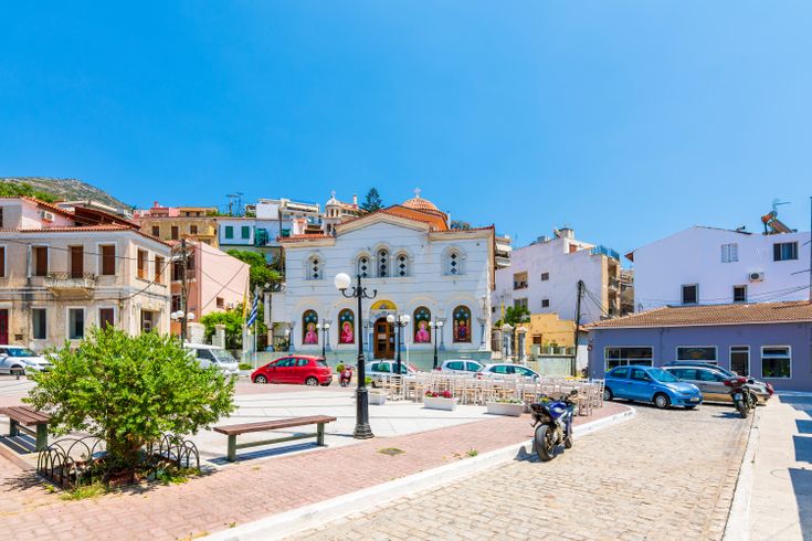 Blick auf die Innenstadt von Vathy mit seinen kleinen bunten Häuser, Sitzmöglichkeiten und einigen Autos.