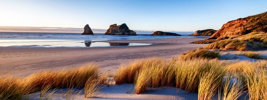 Ein Sandstrand mit Dünen und Blick auf das Meer und Felsen.