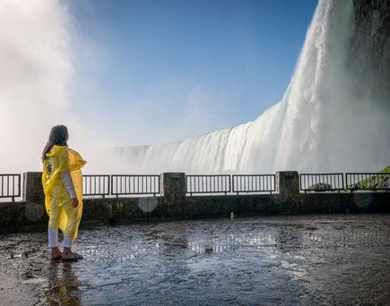 Eine Frau mit gelbem Regencape blickt auf die Niagara Fälle hoch