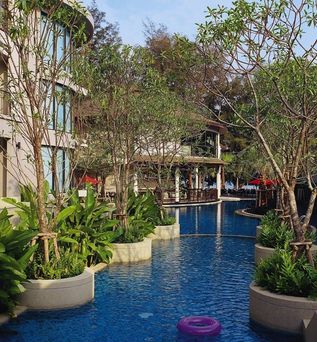 Ein Außenbereich eines Hotels mit einem Swimmingpool, Liegestühlen und einem Garten.