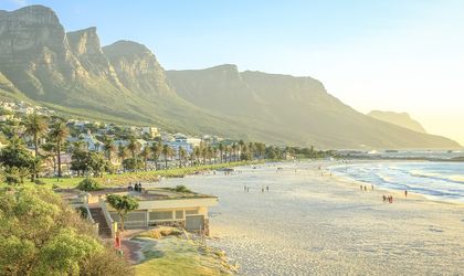 Eine atemberaubende Panoramaansicht der Camps Bay Beach in Kapstadt, Südafrika, mit dem weißen Sandstrand, dem türkisfarbenen Wasser und den majestätischen Zwölf Apostel Bergen im Hintergrund.