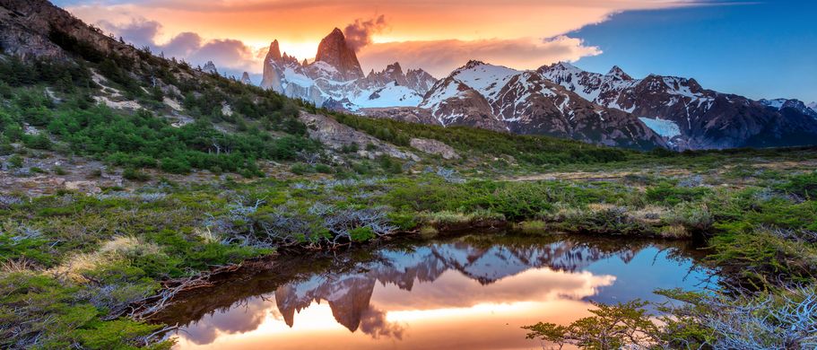 Die dramatische Berglandschaft Patagoniens in Argentinien, mit dem imposanten Fitz Roy Massiv und einem türkisfarbenen Gletschersee im Vordergrund unter einem bewölkten Himmel.