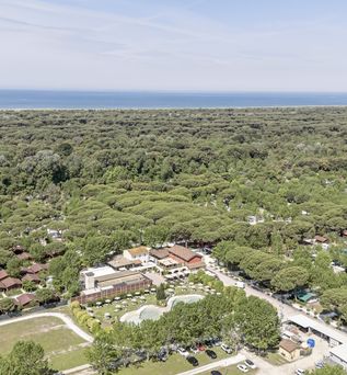 Luftaufnahme eines Ferienresorts mitten in einem dichten Pinienwald mit direktem Zugang zum Meer im Hintergrund.