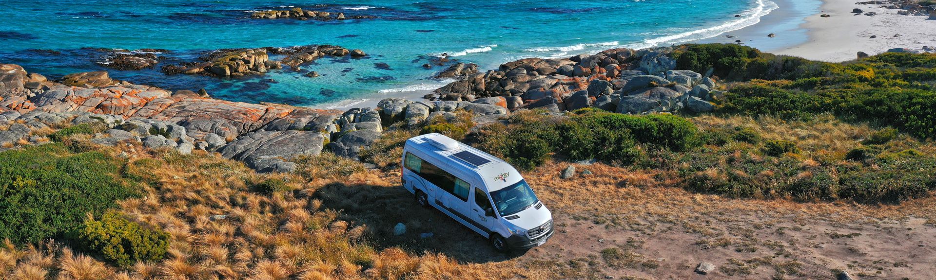 Ein Camper steht an einem Felsigen Strand mit türkisblauem Meer in Australien 