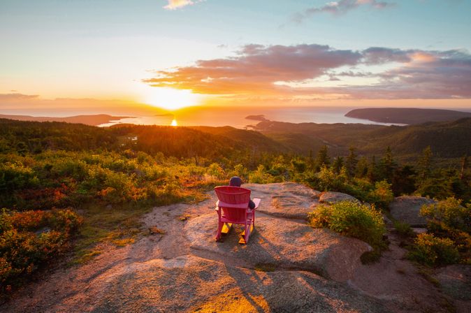 Eine Person sitzt mit dem Rücken in einem roten Stuhl am Franey Trail bei Sonnenuntergang