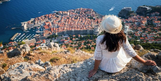 Eine Frau sitzt auf einer Klippe und blickt auf die Stadt Dubrovnik.