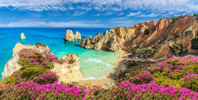 Eine malerische Bucht mit türkisfarbenem Wasser und goldenem Sand, die Praia do Camilo oder Marinha Beach, umgeben von beeindruckenden Felsformationen und grünem Bewuchs.