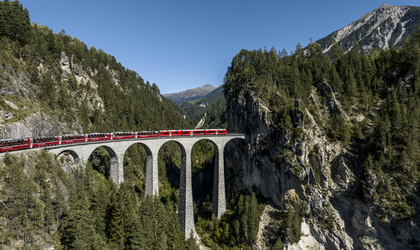 Zug fährt auf einer Brücke durch eine bergige Landschaft mit grüner Natur
