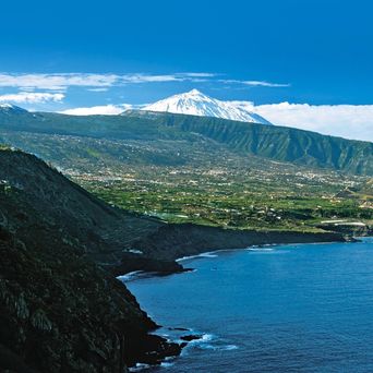 Der majestätische, schneebedeckte Gipfel des Vulkans Teide auf Teneriffa, der sich über einer kargen Vulkanlandschaft und Wolken erhebt, möglicherweise im warmen Licht des Sonnenaufgangs oder Sonnenuntergangs gesehen.