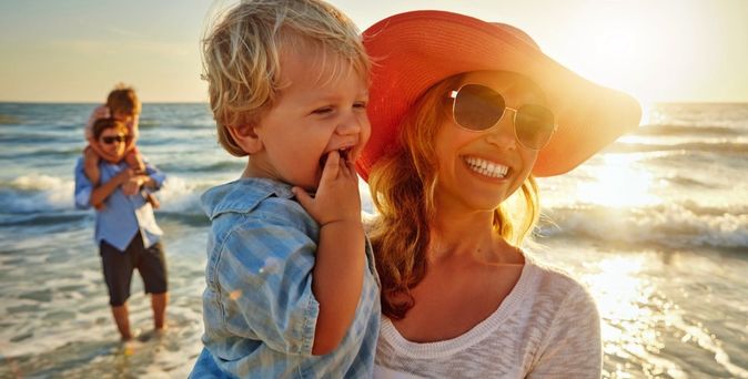 Eine Frau hält ein Kind im Arm am Strand.
