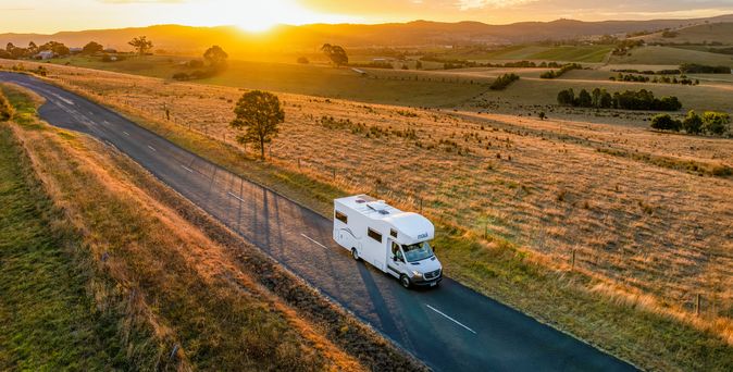 Wohnmobil fährt während Sonnenuntergang entlang einer Straße umgeben von Feldern in Australien 