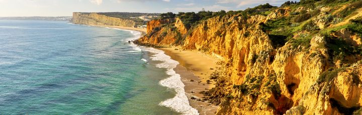 Eine felsige Küstenlinie mit türkisfarbenem Wasser und einem Strand.