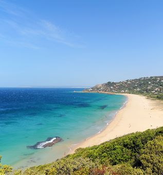 Ein Sandstrand mit türkisfarbenem Wasser und einer grünen Küstenlinie.