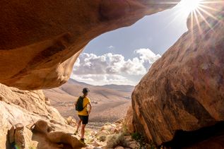 Wanderer steht auf Fuerteventura und blickt in die Ferne in die Sonne