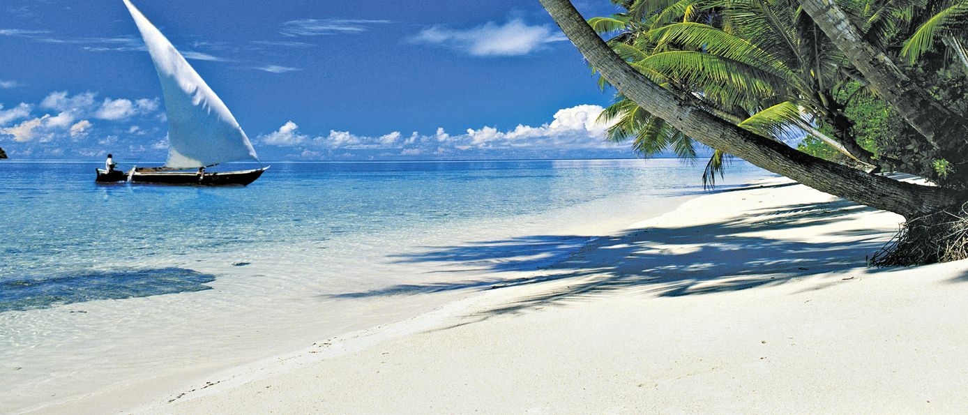Hellblaues Meer und weißer Sand mit Palmen und einem Boot mit Segel im Meer am Serena Beach Resort & Spa Strand in Kenia