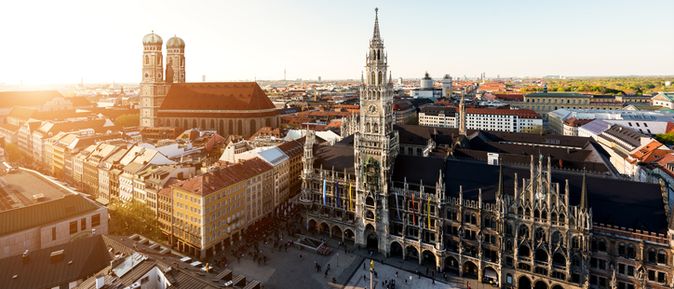 Luftaufnahme des Marienplatzes in München bei Sonnenuntergang mit dem Neuen Rathaus und der Frauenkirche im Hintergrund.