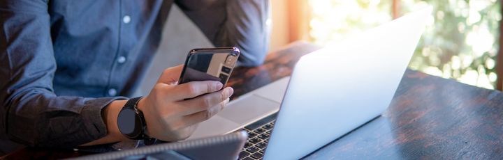 Geschäftsperson arbeitet mit Laptop und Smartphone an einem sonnendurchfluteten Tisch, moderne Arbeitsumgebung.