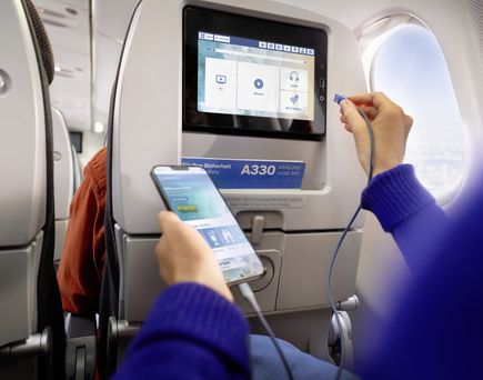 Entertainmentbildschirm im Flugzeug, eine Person schließt Kopfhörer an