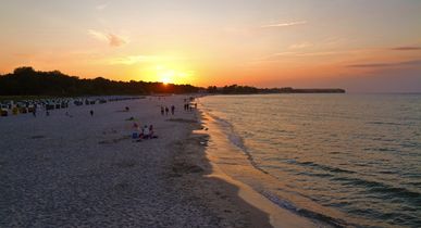 Sonnenuntergang am Sandstrand von Usedom mit Spaziergängern am Wasser.