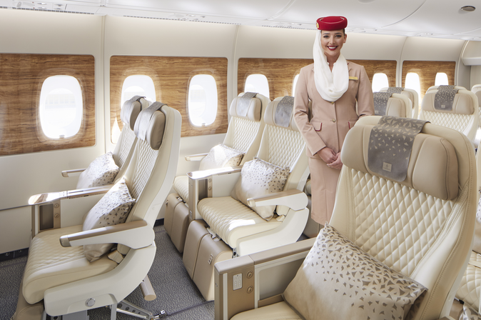 Flugbegleiterin in Emirates-Uniform steht in einer hellen, komfortablen Premiumkabine mit großzügigem Sitzabstand.