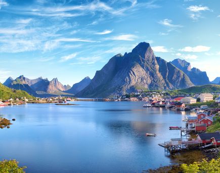 Eine atemberaubende Landschaft der Lofoten in Norwegen, zeigt das malerische Dorf Reine mit seinen roten Fischerhütten, umgeben von majestätischen Bergen, die sich aus dem Meer erheben.