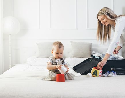 Frau packt koffer und Baby sitzt davor auf dem Bett