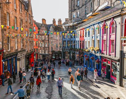 Eine belebte Straße in Edinburgh mit vielen bunten Gebäuden und Menschen.
