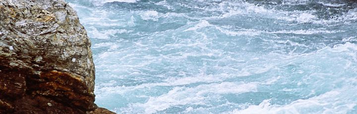 Ein Schlauchboot mit Personen auf einem Fluss, umgeben von Stromschnellen.