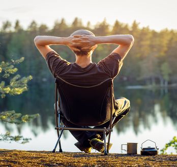Eine Person sitzt entspannt in einem Holzstuhl am Wasser.