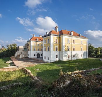 Ein Schloss oder Herrenhaus auf einem Hügel, umgeben von grüner Landschaft.