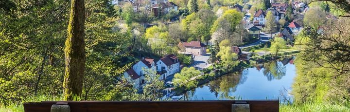 Blick auf eine Bank, welche über den Thüringer Wald zeigt. See, Bäume und blauer Himmel.