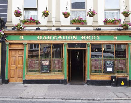 Die traditionelle Fassade des Pubs "Hargadon Bros" mit einer grünen Holzverkleidung, großen Schaufenstern und Blumenkästen unter den Fenstern im oberen Stockwerk. Die Hausnummern "4" und "5" sind deutlich sichtbar.