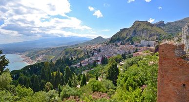 Eine Panoramablick auf die Stadt Taormina, eingebettet in eine grüne Hügellandschaft mit Blick auf das Meer.
