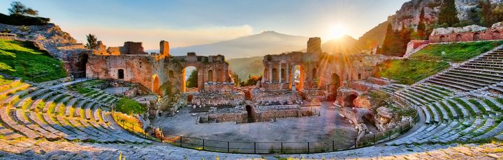 Die Ruinen eines antiken Theaters mit Blick auf die Küste und Berge im Hintergrund.