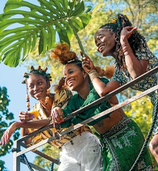 Drei Frauen aus der Karibik stehen unter der Palme und sind fröhlich