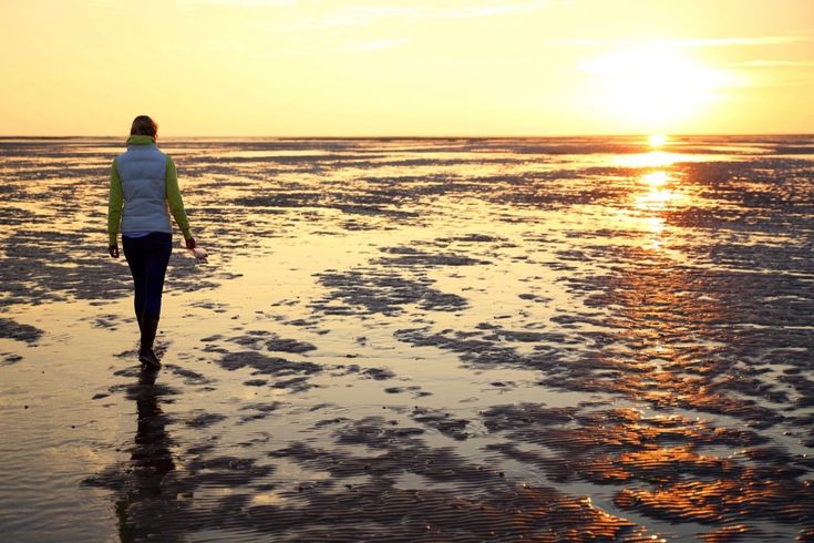 Eine Person geht auf einem Strandweg bei Sonnenuntergang.