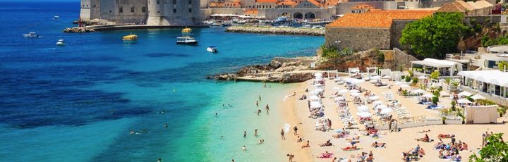 Ein belebter Sandstrand mit vielen Menschen und türkisfarbenem Wasser.
