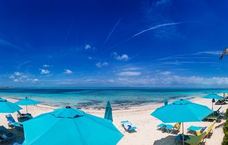 Ein Sandstrand mit türkisfarbenem Wasser, Sonnenschirmen und Liegestühlen.