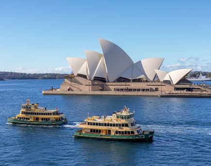 Das Opera House auf Bennelong Point in Sydney Harbour in Australien. Im Vordergrund zwei Schiffe auf dem Wasser.
