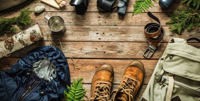 Verschiedene Outdoor-Ausrüstungsgegenstände wie Rucksack, Wanderschuhe und Kamera liegen bereit.