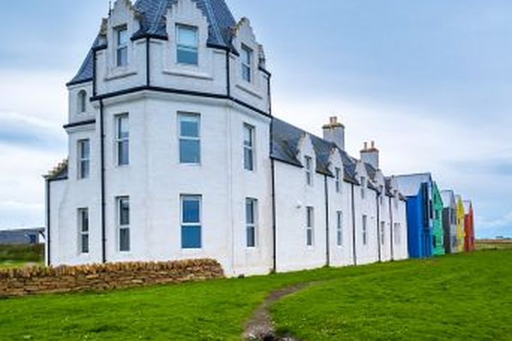 Ein weißes Schloss mit einem spitzen Turm. Das Gebäude ist von grünem Gras umgeben.