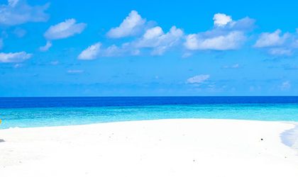 Ein unberührter Sandstrand mit einem einzelnen Sonnenschirm und Liegestühlen unter einem strahlend blauen Himmel. Das türkisfarbene Meer ist ruhig.