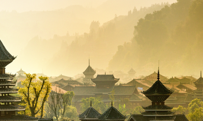 Eine alte chinesische Landschaft mit traditioneller Architektur, die sich in einer gebirgigen Kulisse mit Nebel und üppiger Vegetation befindet.